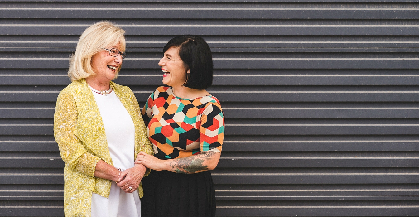 A woman and her mother wearing brightly coloured clothes and laughing.