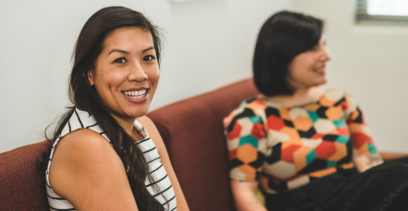 Two women sitting on a couch smiling.